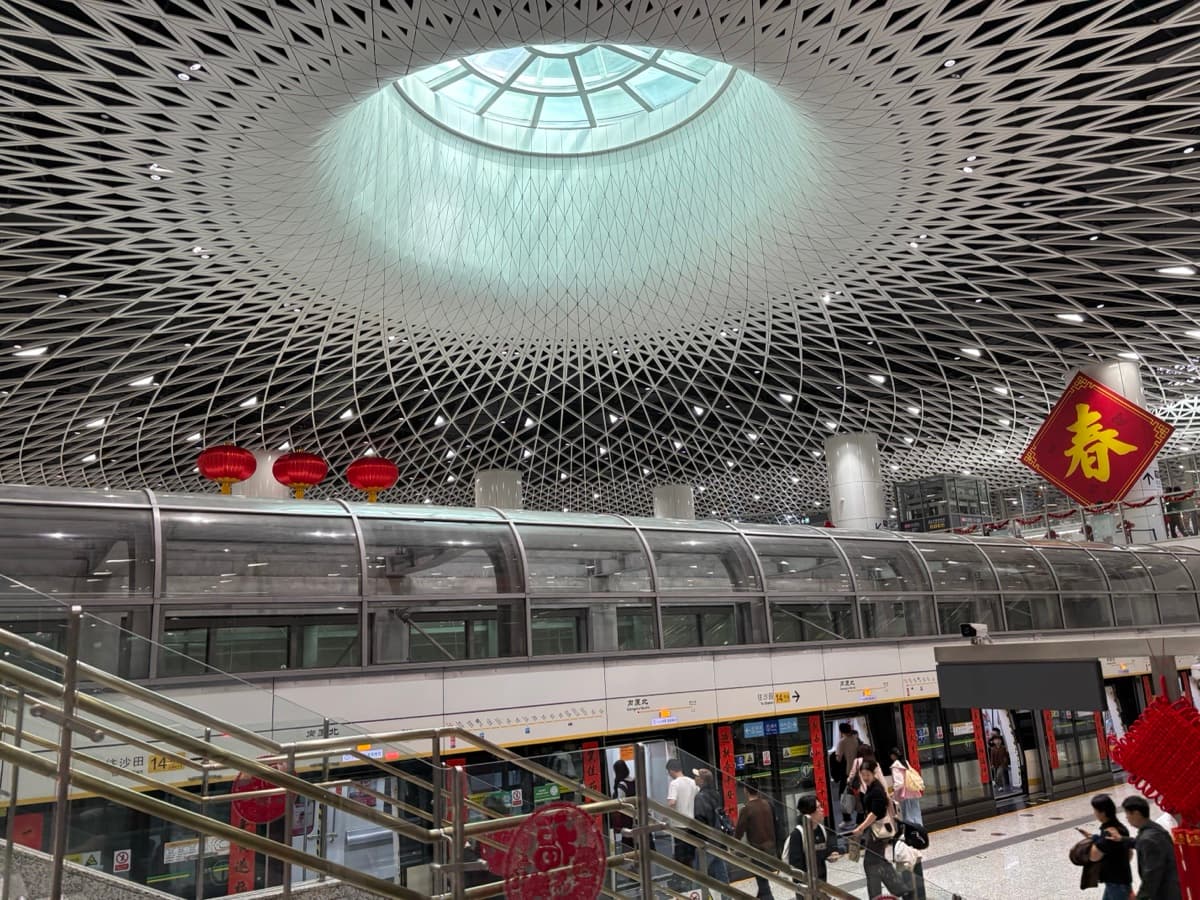 Crowded Shenzhen metro hall with dome ceiling and travelers using payment and navigation apps on their phones